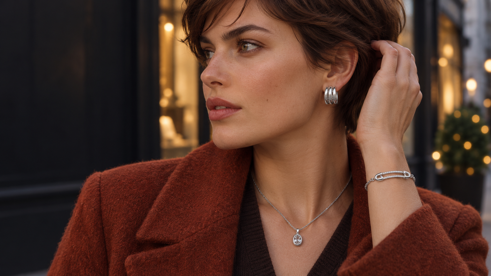 Model in a rust-colored coat wearing silver-tone earrings, a necklace and a bracelet
